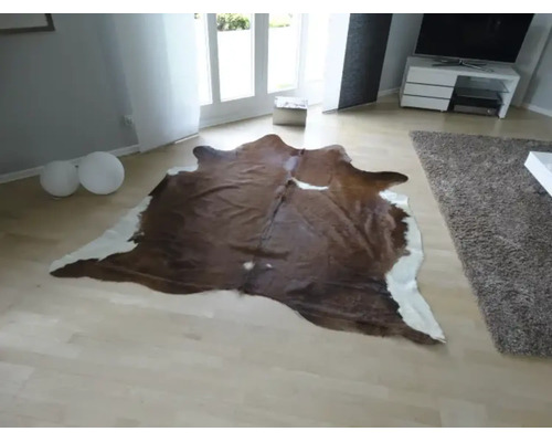 Naturligt formad matta av kohud i ett ljust, modernt inrett vardagsrum med ljust parkettgolv.
