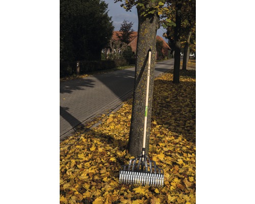 En lövkratta med träskaft lutar mot ett träd mitt i höstlöven.