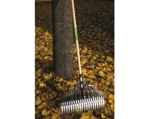 Lövraka i plast med träskaft står mot ett träd mitt bland höstlöv.