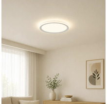 Platt, rund LED-taklampa i ett ljust, minimalistiskt vardagsrum med trämöbler och dekorationer.