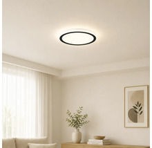 Modern rund LED-taklampa med svart kant i ett ljust, minimalistiskt vardagsrum med vita väggar och ljusa möbler.