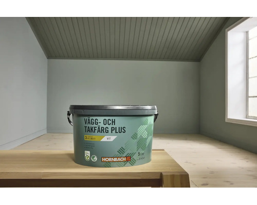 Hornbach vägg- och takfärg Plus hink 5 liter i helmatt vit på ett träbord i ett ljust rum med ett tak av träribbor.