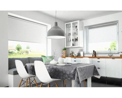 Ljust, modernt kök med vita plisségardiner i fönstren, ett dukat matbord och en grå taklampa.