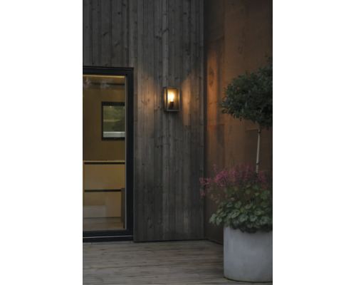 Modern utomhusvägglampa med glas på en träfasad på en terrass med växter.
