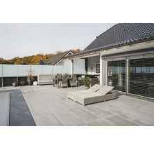 Modern terrass med ljusgrå golvplattor, ljusa rottingträdgårdsmöbler, solsängar och insynsskydd av glas.