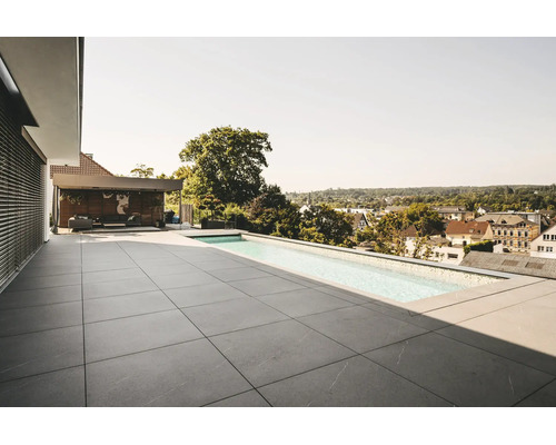 Modern takterrass med stora grå stenplattor och en smal infinitypool. Övertäckt loungeyta i bakgrunden. Ljus och rymlig atmosfär.