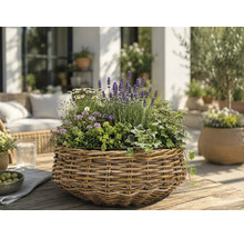 Flätad korg med lavendel, murgröna och vita blommor på ett träbord på en ljus, organiserad terrass med trädgårdsmöbler.
