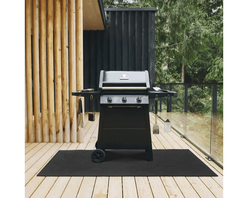 Svart gasolgrill med tre brännare och grillredskap på en svart grillmatta på en träterrass.