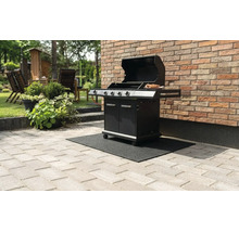 Svart gasolgrill med öppet lock på en svart grillmatta på en stenterrass intill en tegelvägg.