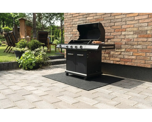 Svart gasolgrill med öppet lock på en svart grillmatta på en stenterrass intill en tegelvägg.