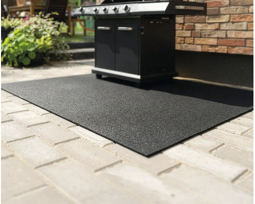 Svart strukturerad grillmatta som skyddar marken, placerad på en stenlagd uteplats under en gasolgrill.
