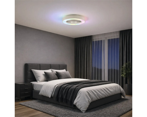 Modern takfläkt med färgad LED-ljusring i ett sovrum med grå klädd säng, mörka gardiner och matta.