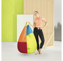 En kvinna står bredvid en stor, droppformad, flerfärgad saccosäck med handtag i en modern studiomiljö med träelement.
