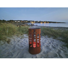 Eldstad i metall med utskärningar på stranden med glöd och Landmann logotyp i skymningen.