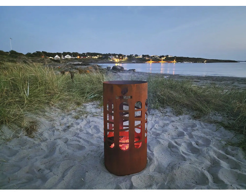 Eldstad i metall med utskärningar på stranden med glöd och Landmann logotyp i skymningen.