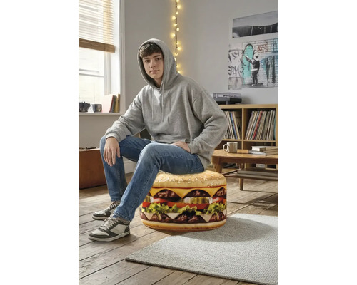 En tonåring sitter på en rund sittpuff formad som en hamburgare i ett ljust rum med trägolv.