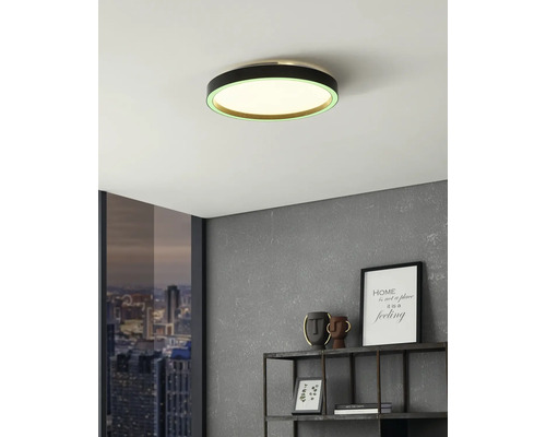 Modern rund LED-taklampa med svart ram och grön ljusring i ett rum med grå vägg och metallhylla.