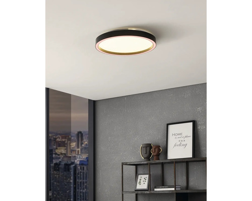 Rund LED-taklampa med svart hölje i ett modernt inrett rum med grå vägg och fönster med stadsutsikt.