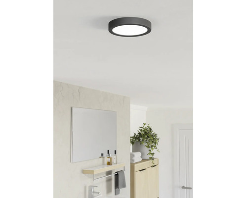 Rund LED-taklampa med mörk ram i ett ljust, modernt badrum med spegel, grön växt och träskåp.