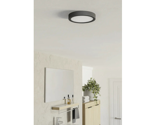 Rund LED-taklampa i ett ljust, modernt badrum med spegel, träskåp och krukväxt.
