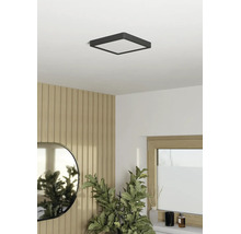 Fyrkantig LED-taklampa i ett ljust, modernt rum med väggpaneler i trälook, en oval spegel och en krukväxt.