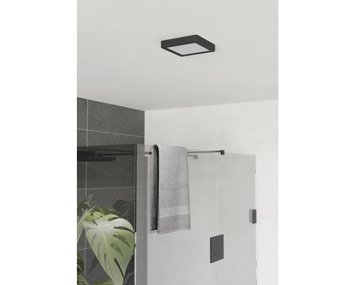 Modernt badrum med kvadratisk svart LED-taklampa, duschvägg i glas, grått kakel och en grön växt.