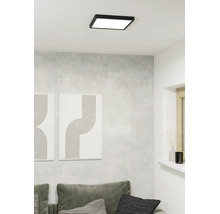 Kvadratisk LED-taklampa med svart ram på ett vitt tak i ett modernt vardagsrum med grå vägg och soffa.