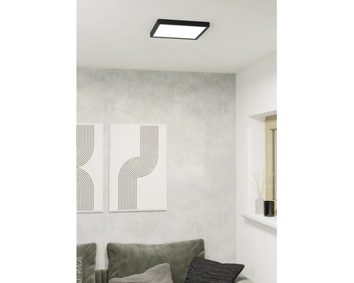 Kvadratisk LED-taklampa med svart ram på ett vitt tak i ett modernt vardagsrum med grå vägg och soffa.