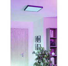 Kvadratisk LED-takpanel i ett vardagsrum med hylla, dörr och krukväxt, för stämningsfull rumsbelysning.