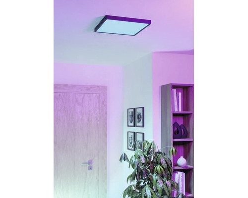 Kvadratisk LED-takpanel i ett vardagsrum med hylla, dörr och krukväxt, för stämningsfull rumsbelysning.
