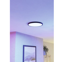 Rund LED-taklampa med svart ram i ett modernt rum med lila ljus och en tavla på väggen.