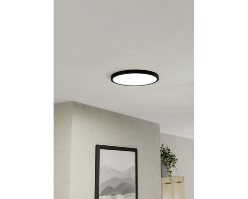 Platt, rund LED-taklampa med svart ram, monterad i taket i ett ljust vardagsrum.