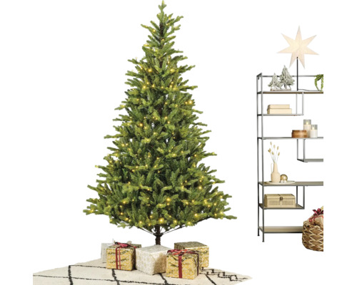 Konstgjord julgran med varmvit LED-belysning, julklappar och en modern metallhylla med juldekorationer på en matta.