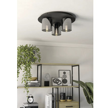 Modern taklampa med metallbas och glasskärmar i ett ljust rum med en dekorativ hylla och krukväxter.