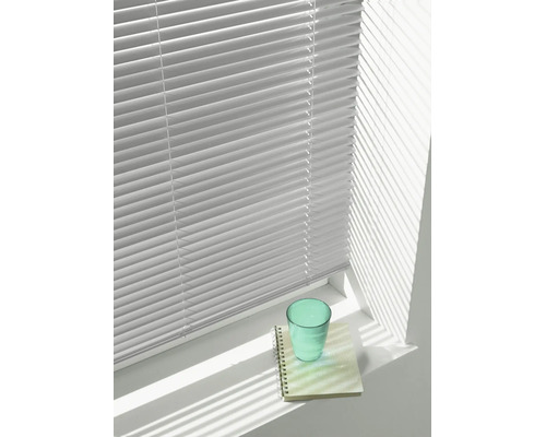 Persienn med horisontella lameller framför ett fönster, som kastar skuggor på en fönsterbräda med ett glas och ett anteckningsblock.
