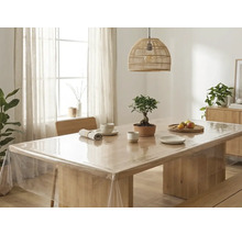 Genomskinlig bordsduk av plast på ett ljust träbord i en ljus, organiserad matsal med en flätad lampa och en bonsai.