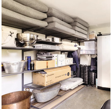 Organiserat hyllsystem i metall med diverse lådor, kuddar och hushållsföremål i en källare eller ett garage.