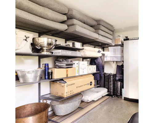 Organiserat hyllsystem i metall med diverse lådor, kuddar och hushållsföremål i en källare eller ett garage.