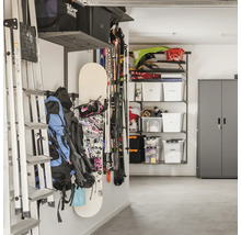 Organiserat garage med vägghyllsystem, stege, snowboard, skidor, ryggsäckar och förvaringslådor i ett metallskåp.