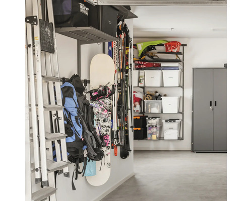 Organiserat garage med vägghyllsystem, stege, snowboard, skidor, ryggsäckar och förvaringslådor i ett metallskåp.