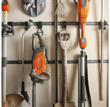 Organiserade trädgårdsredskap på en väggskena med Husqvarna logotyp, inklusive häcksax, röjsåg, spade och sprutlans.