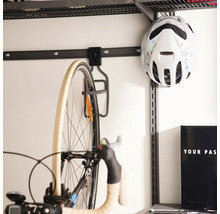 Väggmonterat cykelupphängningssystem med metallkrok för cyklar och en cykelhjälm på en väggskena i ett garage.