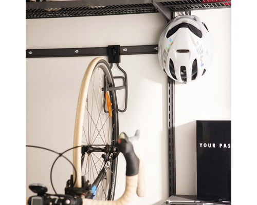 Väggmonterat cykelupphängningssystem med metallkrok för cyklar och en cykelhjälm på en väggskena i ett garage.