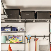 Organiserat trådhyllsystem i ett garage med förvaringslådor, verktyg och campingutrustning monterat på en vägg.