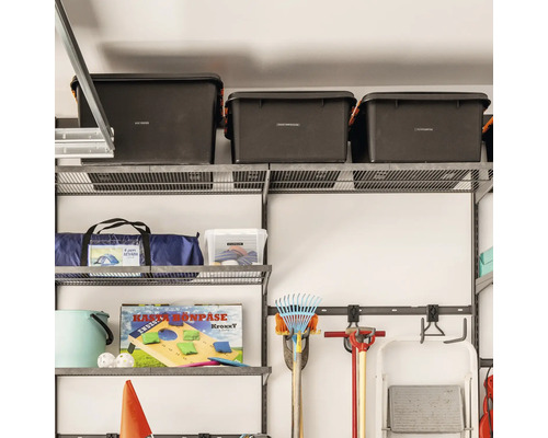 Organiserat trådhyllsystem i ett garage med förvaringslådor, verktyg och campingutrustning monterat på en vägg.