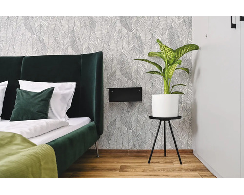 Modernt sovrum med fiber-tapet med bladmonster, stoppad sang, sängbord och krukväxt.