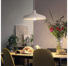 Modern pendellampa ovanför ett matbord med en blombukett och dekoration i bakgrunden i ett ljust vardagsrum.