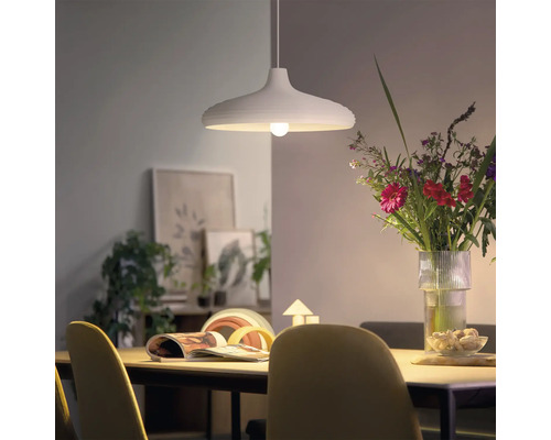 Modern pendellampa ovanför ett matbord med en blombukett och dekoration i bakgrunden i ett ljust vardagsrum.