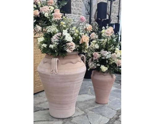 Två stora terrakottaamforer med blomsterarrangemang på ett stengolv.