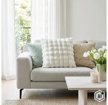 Ett ljust vardagsrum med en soffa dekorerad med tre olika prydnadskuddar samt ett soffbord med en vas fylld med blommor. (Image AI modified or generated)